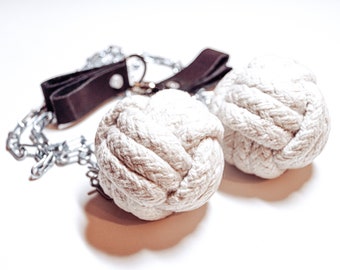 May include: Two white rope balls attached to a brown leather strap and a silver chain. The balls are made of tightly woven rope and are used for fire dancing.