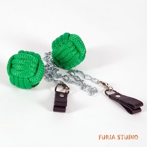 May include: Two green rope balls connected by a silver chain with brown leather handles. The balls are made of knotted rope and are used for fire dancing.
