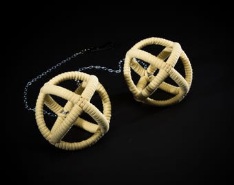 May include: Two beige, spherical objects with a woven, cage-like design, connected by a silver chain. The spheres are set against a black background, creating a striking contrast. The texture of the spheres appears soft and plush.