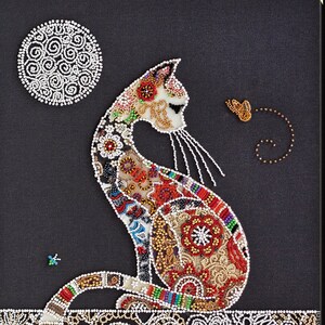 May include: A beaded cat with a colorful, patterned design sits on a beaded surface. The cat is looking to the right, and there is a beaded moon and a beaded butterfly in the background.