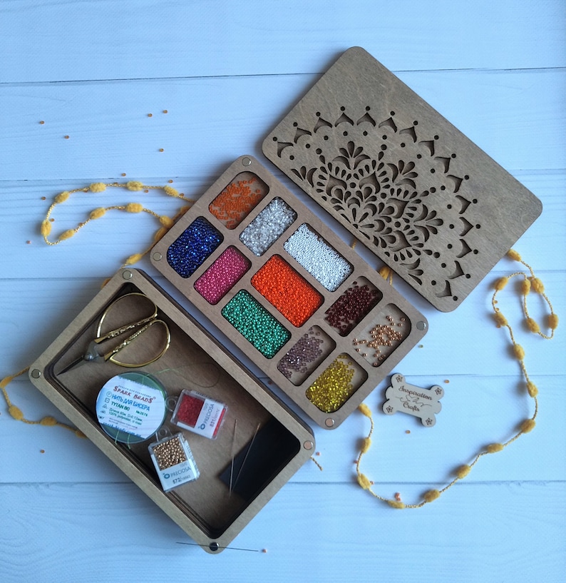 Puede incluir: Una caja de madera con un dise&ntilde;o de mandala en la tapa. La caja tiene 10 compartimentos para guardar cuentas. La caja tambi&eacute;n incluye un carrete de hilo, agujas y un par de tijeras peque&ntilde;as. La caja est&aacute; etiquetada como "Inspiration by Crafts".