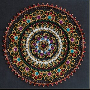 Könnte beinhalten: Ein farbenfrohes Mandala-Design, das mit Perlen und Strasssteinen erstellt wurde. Das Design zeigt ein kreisförmiges Muster mit mehreren Schichten von komplizierten Details. Die Farben umfassen Rot, Gold, Grün, Blau, Lila und Weiß.