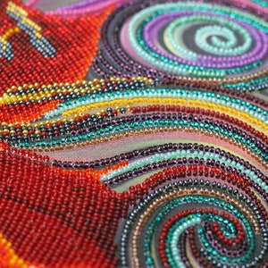 May include: Close-up of a colorful beaded artwork with a swirling pattern. The beads are arranged in a variety of colors, including red, orange, yellow, green, blue, and purple. The artwork is created on a dark background.