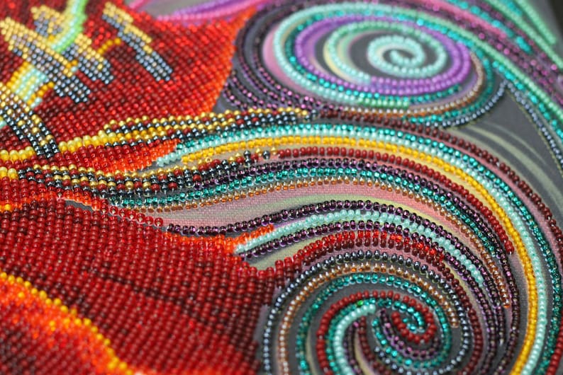 May include: Close-up of a colorful beaded artwork with a swirling pattern. The beads are arranged in a variety of colors, including red, orange, yellow, green, blue, and purple. The artwork is created on a dark background.