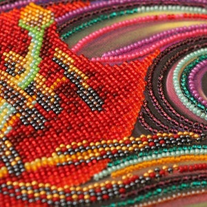 May include: Close-up of a beaded artwork with a swirling pattern of red, orange, yellow, green, blue, purple, and black beads.
