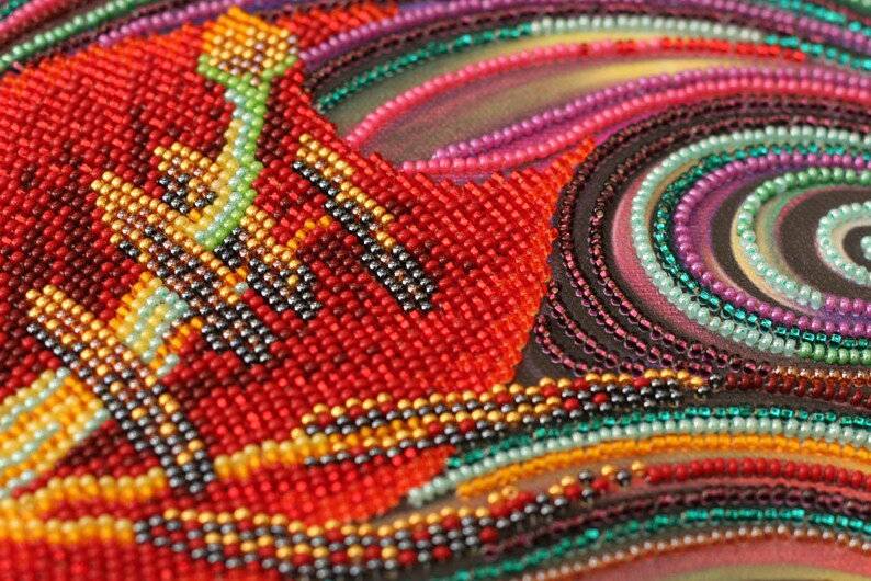 May include: Close-up of a beaded artwork with a swirling pattern of red, orange, yellow, green, blue, purple, and black beads.
