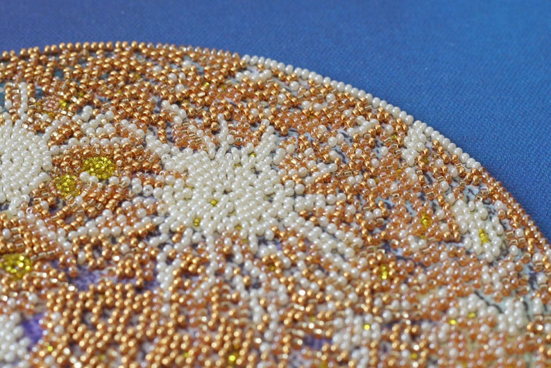 May include: Close-up of a beaded design with white, gold, and yellow beads. The beads are arranged in a circular pattern, creating a floral motif.