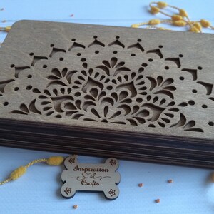 Puede incluir: Una caja de madera con un dise&ntilde;o de mandala decorativo cortado en la parte superior. La caja est&aacute; hecha de m&uacute;ltiples capas de madera y tiene un acabado marr&oacute;n. Una peque&ntilde;a etiqueta de madera con el texto "Inspiration Crafts" est&aacute; en primer plano.