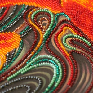 May include: Close-up of a beaded artwork with swirling patterns in shades of red, orange, green, and black.