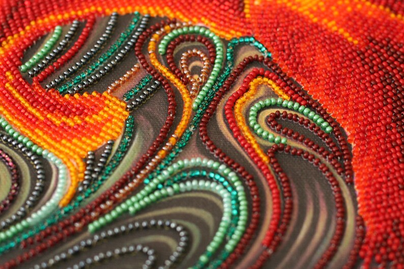 May include: Close-up of a beaded artwork with swirling patterns in shades of red, orange, green, and black.