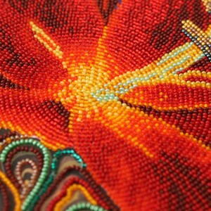 May include: Close-up of a beaded artwork depicting a red flower with yellow and blue accents. The beads are arranged in a circular pattern, creating a textured and intricate design.
