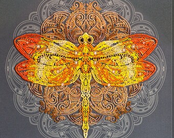 May include: A close-up of a beaded dragonfly with orange, yellow, and brown accents. The dragonfly is centered on a mandala-like design with intricate details.