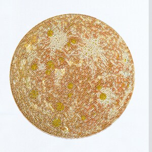 May include: A close-up of a circular beaded artwork depicting a planet with a textured surface. The artwork is made with small, white, gold, and orange beads.