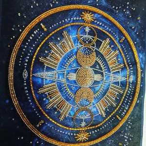 Pode incluir: Um design celestial bordado sobre um fundo azul escuro. O design circular apresenta contas douradas e prateadas, retratando estrelas, sóis, luas e padrões geométricos. A obra de arte tem uma aparência detalhada e texturizada.