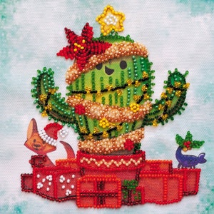May include: A green cactus wearing a red and gold beaded garland and a star on top. The cactus is sitting on a red and white beaded base with two small beaded animals on either side.