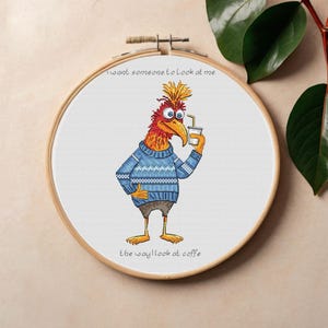 May include: Cross-stitch embroidery in a wooden hoop features a cartoon bird with a yellow crest, blue sweater, and shorts, holding a coffee cup. The text reads "I want someone to look at me the way I look at coffee."