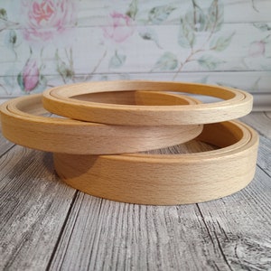 Puede incluir: Tres aros de bordado de madera de diferentes tamaños apilados uno encima del otro. Los aros son de madera natural y tienen un acabado liso.
