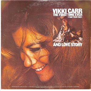 May include: Vintage vinyl record album cover featuring Vikki Carr. The album is titled "The First Time Ever (I Saw Your Face) and Love Story." The cover art showcases a close-up of a woman's face with long, reddish-brown hair and a warm smile.