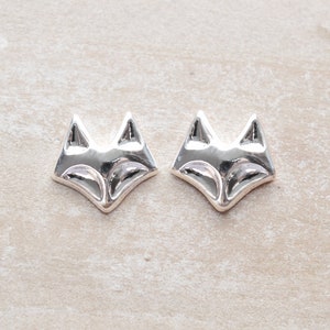 May include: A pair of silver fox head stud earrings. The fox heads are facing forward with a simple design.