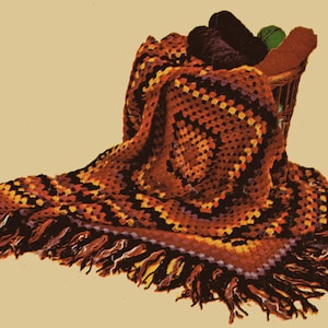 May include: A crocheted throw blanket with a geometric pattern in shades of orange, yellow, black, and purple. The blanket has a fringe border and is draped over a basket.