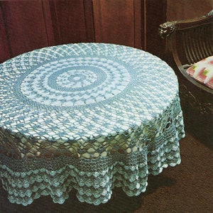 Puede incluir: Un mantel de crochet azul claro con un diseño circular en el centro. El mantel está puesto sobre una mesa redonda y tiene un borde festoneado.