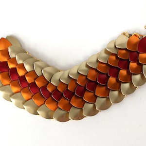 May include: A gold, orange, and red metal bracelet with a scale-like design. The bracelet has a clasp closure.