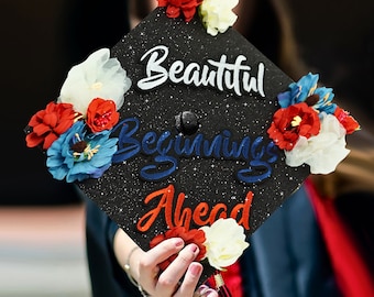 May include: A black graduation cap decorated with red, white, and blue flowers and the words "Beautiful Beginnings Ahead".