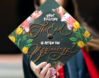 May include: A graduation cap with floral accents and the text "What Feels Like The End Is Often The Beginning!" in gold glitter. The cap is dark green with pink and yellow flowers.