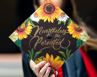 Peut inclure: Un bonnet de graduation noir avec un motif floral et des lettres dorées scintillantes qui disent "Nevertheless, the Persisted".
