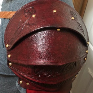 Può includere: Un'armatura per spalla in pelle bordeaux con rivetti dorati e disegni di gufi in rilievo.