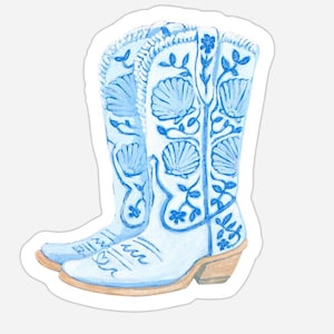 Könnte beinhalten: Ein Paar hellblaue und weiße Cowboy-Stiefel mit Muschel- und Blumendesigns. Die Stiefel haben einen hellbraunen Absatz und sind mit aufwendigen blauen Mustern verziert. Das Gesamtdesign erinnert an Küstendekoration.