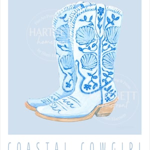 Könnte beinhalten: Aquarellillustration von zwei hellblauen Cowboy-Stiefeln mit Muschel- und Blumenmotiven. Die Stiefel haben hellbraune Absätze und sind vor einem hellblauen Hintergrund platziert. Der Text "COASTAL COWGIRL" steht unten.