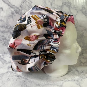 May include: A pink satin shower cap with a print of fashion magazines, shoes, and the words "Fashion Looky Glamour" and "Style Mistabas".