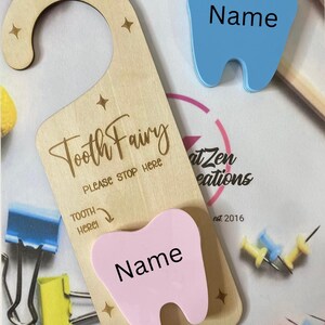 May include: A wooden door hanger with the text "Tooth Fairy Please Stop Here" and a space for a tooth. The hanger has a pink tooth with the word "Name" written on it.