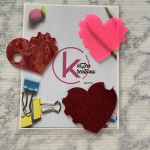 May include: Three heart-shaped paper cutouts with different textures and colors. The hearts are red, pink, and a sparkly red. The hearts are on a white background with the text "Kat Zen Creations est 2016".