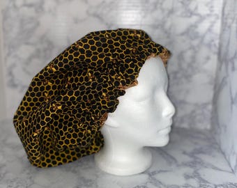 May include: A black and yellow shower cap with a honeycomb pattern and small bee illustrations. The cap is made of satin and has an elastic band.
