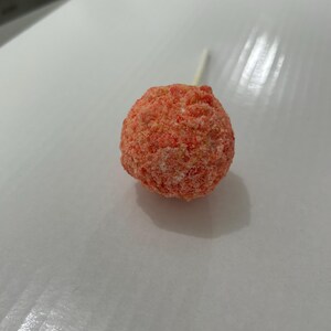 May include: A pink cake pop with a white stick. The cake pop is covered in sprinkles.