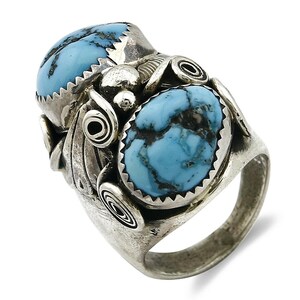 May include: A silver ring featuring two oval-shaped, light blue turquoise stones with dark matrix patterns. The ring has a detailed, ornate design with spiral and leaf-like accents, and a textured band.