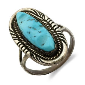 Op de afbeelding: Ovale turkoois ring met een zilveren zetting. De turkoois steen is lichtblauw van kleur met donkerblauwe insluitsels. De zilveren zetting heeft een gedetailleerd ontwerp met een touwachtige rand en decoratieve accenten.