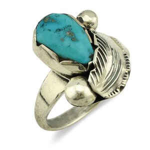May include: A silver ring featuring a large, teardrop-shaped turquoise stone. The ring has a detailed feather design and two small, round accents. The turquoise stone is a vibrant blue-green color.