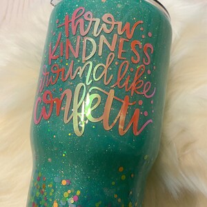 May include: A teal green tumbler with glitter and confetti. The tumbler has the text "Throw kindness around like confetti" in a pink and orange gradient.