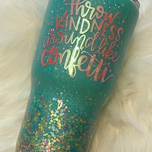 May include: A teal green tumbler with a glitter finish and a quote that reads "Throw kindness around like confetti".