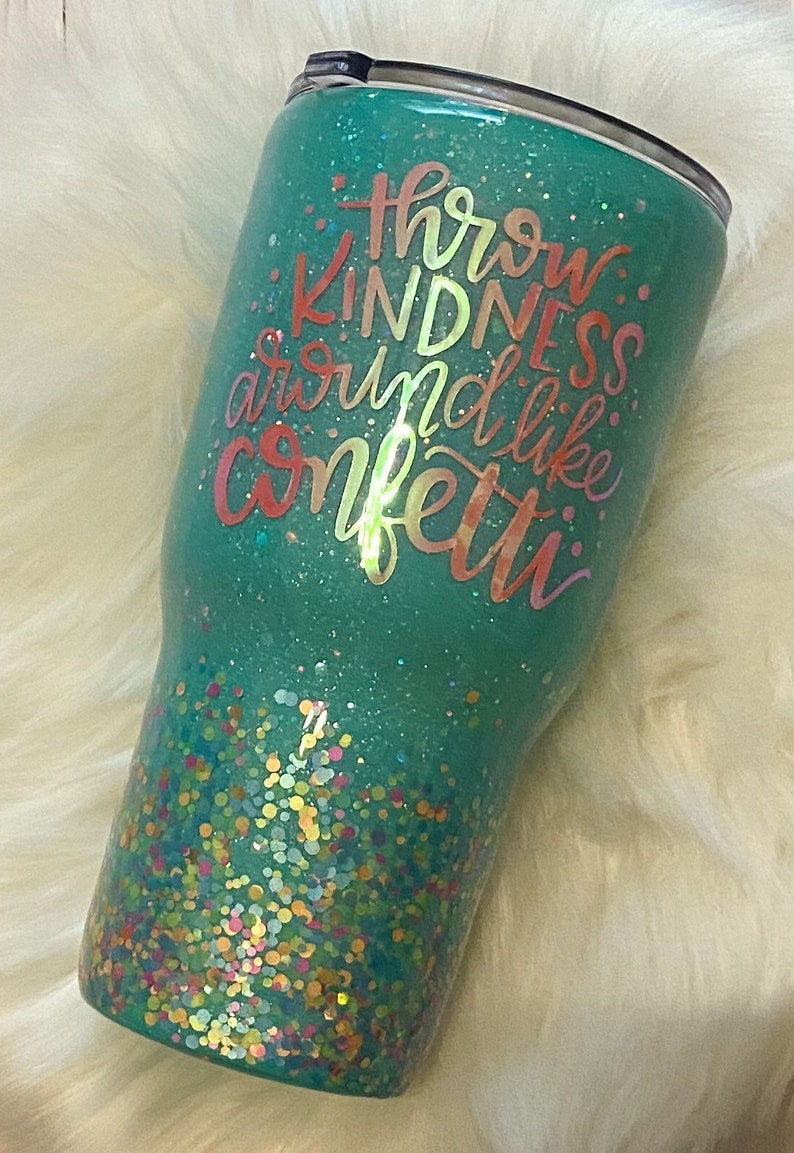 May include: A teal green tumbler with a glitter finish and a quote that reads "Throw kindness around like confetti".
