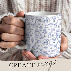 May include: White ceramic mug featuring a blue and white safari-themed pattern with elephants, giraffes, hot air balloons, and trees. The mug is held by a person wearing a cream-colored sweater. The text "CREATE mugs" is at the bottom.