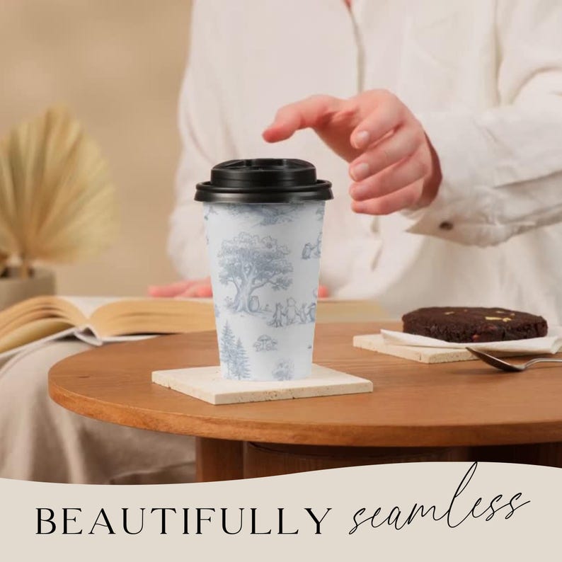 May include: A white travel mug with a black lid, featuring a blue and white pastoral scene design. The mug sits on a square coaster on a wooden table. The text "BEAUTIFULLY seamless" is at the bottom of the image.