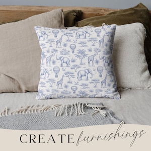 May include: A square throw pillow with a blue and white safari pattern featuring elephants, giraffes, hot air balloons, and trees. The pillow is placed on a bed with other pillows and a blanket. The words "CREATE furnishings" are at the bottom.