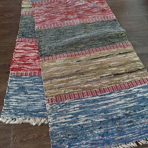 Könnte beinhalten: Ein gewebter Teppich mit einem Streifenmuster in Rot-, Blau-, Braun- und Weißtönen. Der Teppich hat an beiden Enden Fransen.