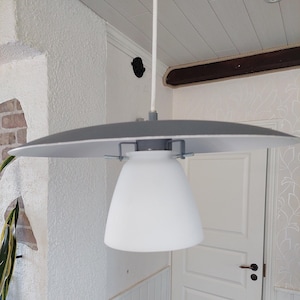May include: A white ceiling light fitting with a grey, saucer-shaped shade and a white, bell-shaped diffuser.