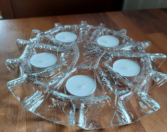 May include: A clear glass candle holder with a textured, wave-like design. The holder has five individual candle wells and is perfect for tea lights.