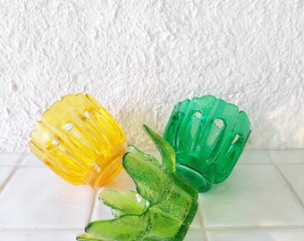May include: Three glass candle holders in the shape of a flower. One is yellow, one is green, and one is a darker shade of green.
